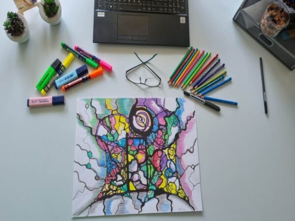 Bunte Neurographik-Zeichnung auf Papier mit schwarzen Linien, umgeben von Buntstiften, Filzstiften, Brille und Laptop auf Schreibtisch